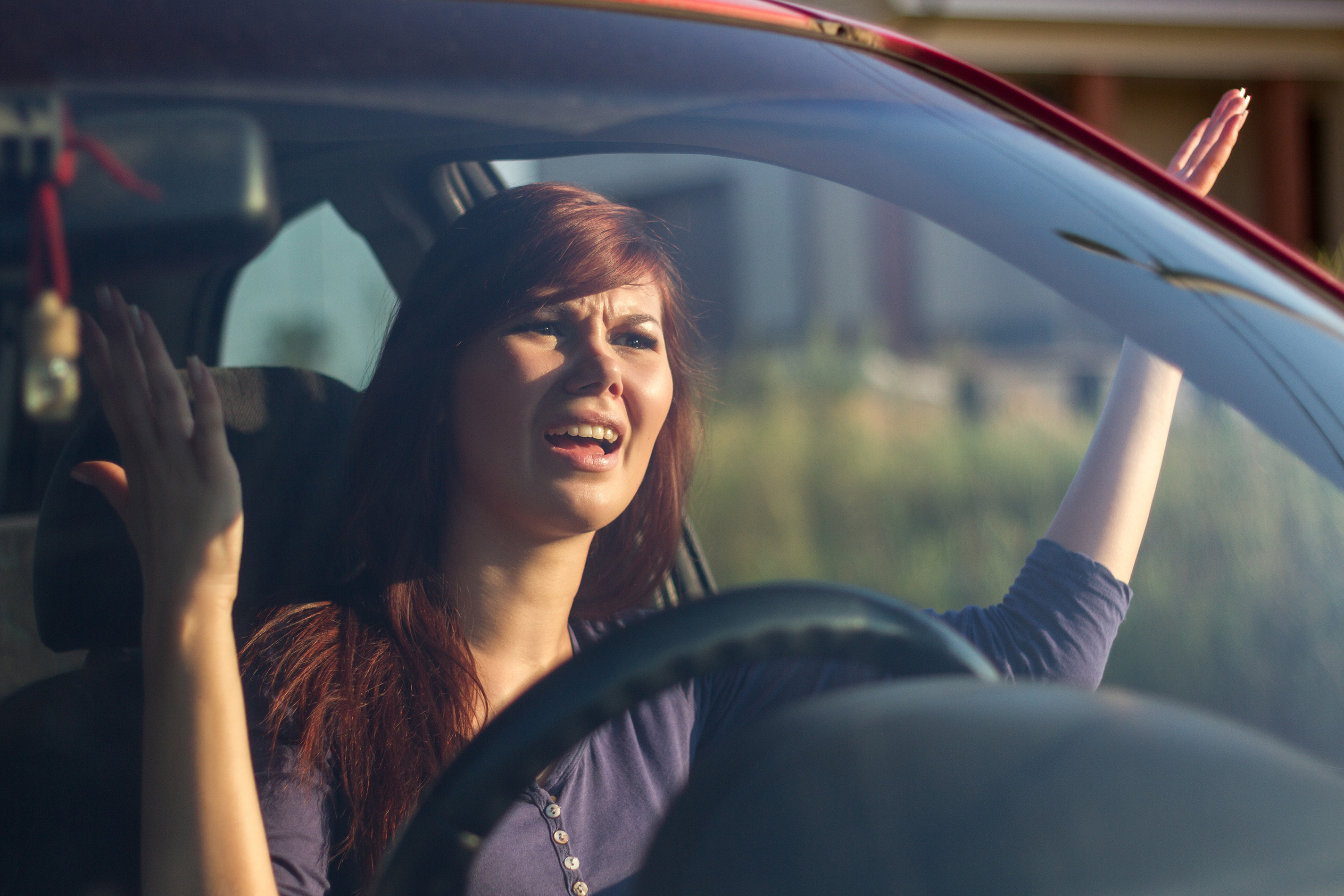 Closeup portrait, angry young sitting woman pissed off by drivers in front of her and gesturing with hands. Road rage traffic jam concept